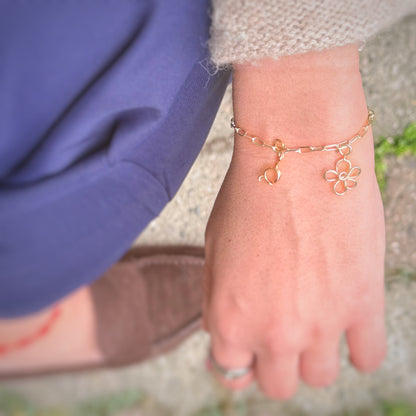 Due charm fiore agganciati a un bracciale a catena, indossati al polso — Trame gioielli