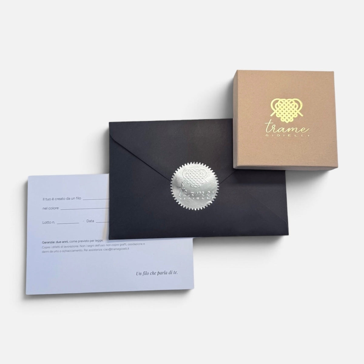 Scatolina con il logo in oro, busta nera chiusa dal sigillo argentato e card della garanzia: la confezione in cui arriva ogni gioiello — Trame gioielli