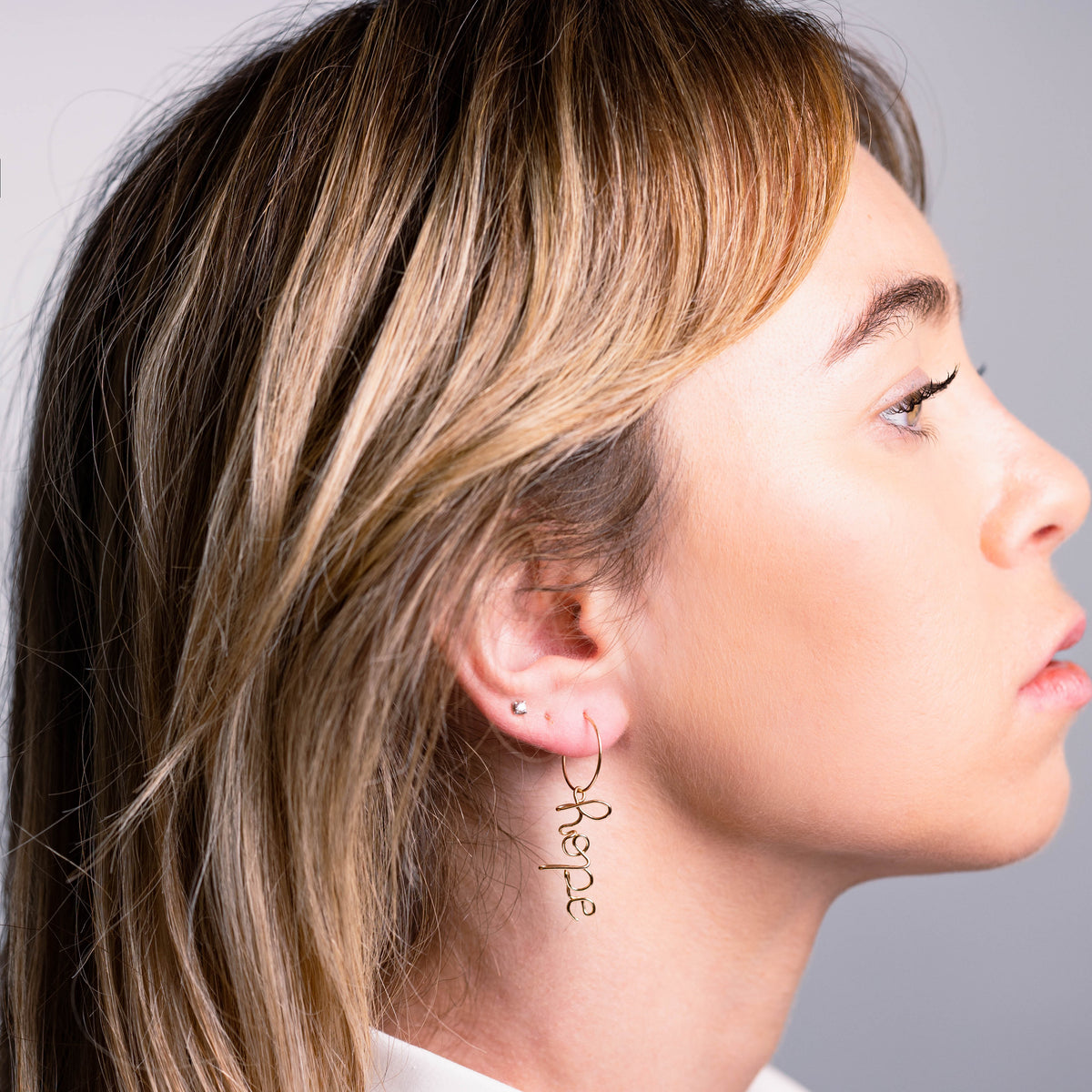 Ragazza di profilo con orecchino a cerchio e il Segno Parola – Il Sussurro agganciato al cerchio — Trame gioielli